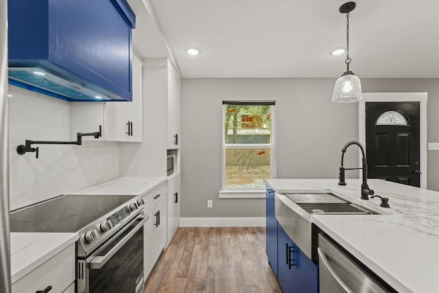 kitchen featuring white cabinets, light hardwood / wood-style flooring, appliances with stainless steel finishes, wall chimney range hood, and blue cabinets