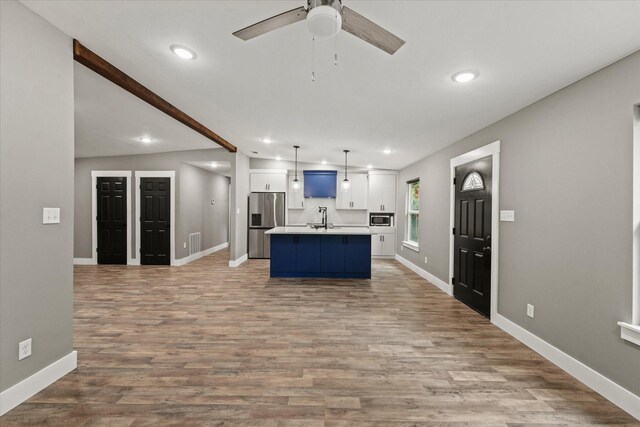 kitchen featuring light wood-type flooring, appliances with stainless steel finishes, decorative light fixtures, and a center island with sink