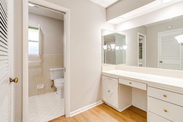 bathroom featuring toilet, a wainscoted wall, wood finished floors, vanity, and tile walls