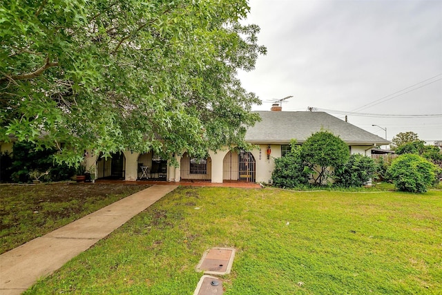 obstructed view of property featuring roof with shingles, a front lawn, a chimney, and stucco siding