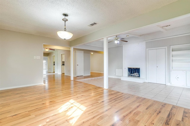 unfurnished living room with a textured ceiling, light wood finished floors, a fireplace, and visible vents