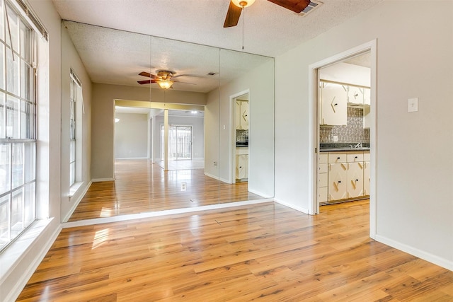 empty room with ceiling fan, light wood-style flooring, and a textured ceiling