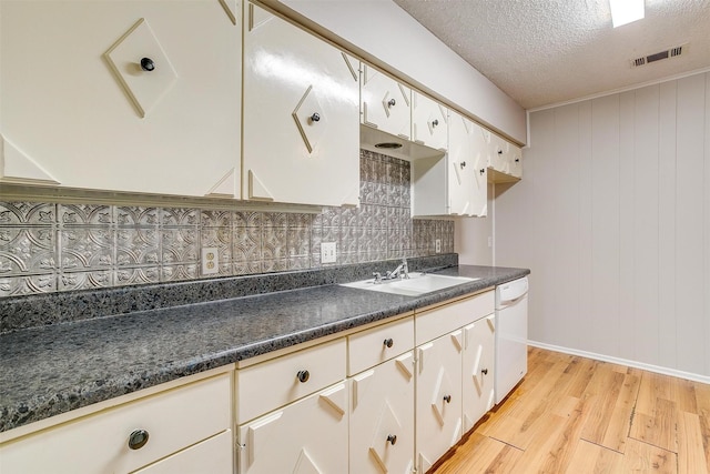 kitchen featuring white dishwasher, a sink, visible vents, light wood finished floors, and dark countertops