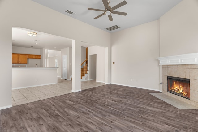 unfurnished living room with light wood-type flooring, ceiling fan, and a tiled fireplace