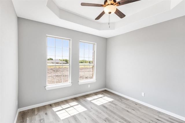 spare room featuring light wood-type flooring, a tray ceiling, and ceiling fan