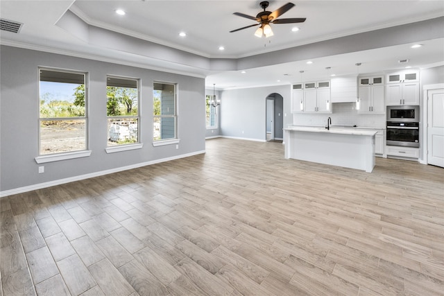 unfurnished living room featuring ceiling fan with notable chandelier, ornamental molding, a raised ceiling, and light hardwood / wood-style flooring