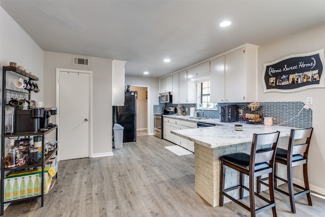 kitchen featuring appliances with stainless steel finishes, white cabinetry, a breakfast bar, kitchen peninsula, and light hardwood / wood-style flooring