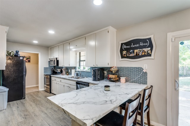 kitchen with white cabinets, sink, kitchen peninsula, appliances with stainless steel finishes, and light wood-type flooring