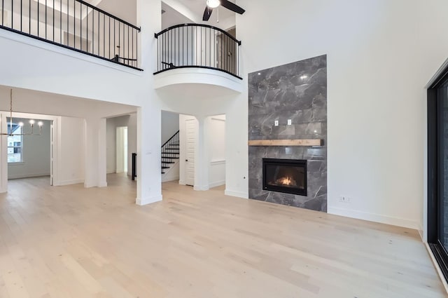 unfurnished living room featuring a premium fireplace, ceiling fan with notable chandelier, a high ceiling, and light wood-type flooring