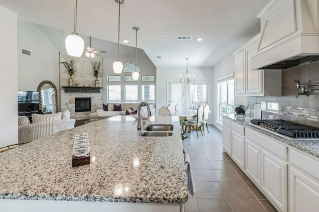 kitchen with a kitchen island with sink, white cabinetry, premium range hood, sink, and a stone fireplace