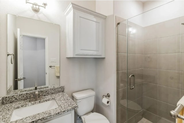 bathroom featuring a shower with shower door, toilet, and vanity