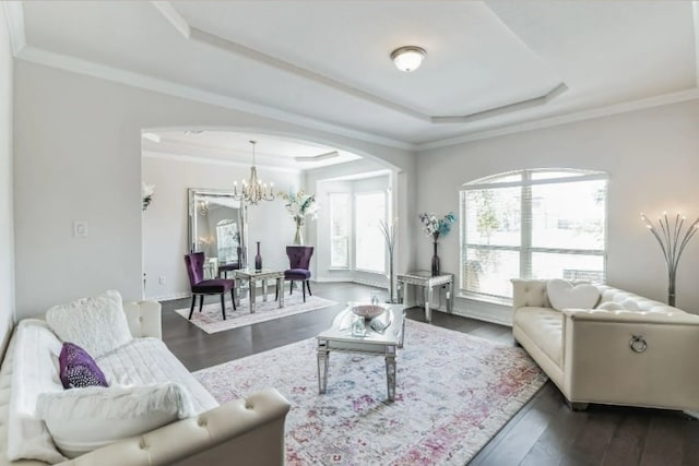 living room featuring dark wood-type flooring, a tray ceiling, an inviting chandelier, and ornamental molding