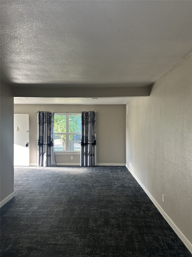 spare room featuring dark carpet, a textured ceiling, and beamed ceiling