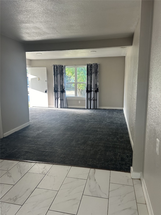 unfurnished room featuring a textured ceiling, carpet flooring, and beam ceiling