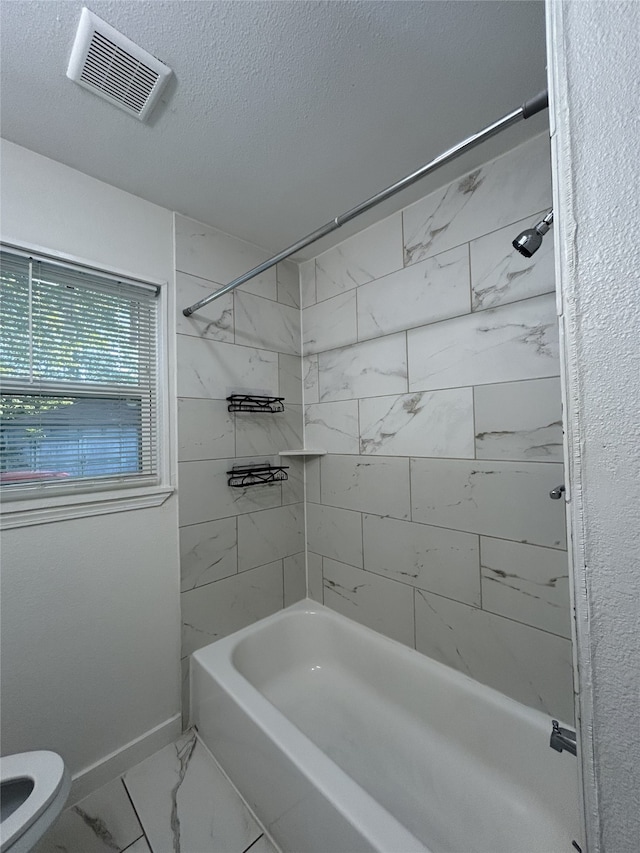 bathroom featuring tiled shower / bath, a textured ceiling, and toilet