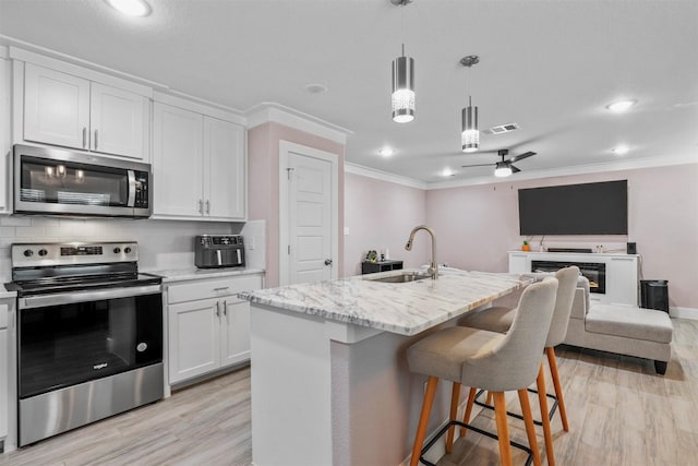 kitchen with open floor plan, appliances with stainless steel finishes, a center island with sink, and white cabinetry