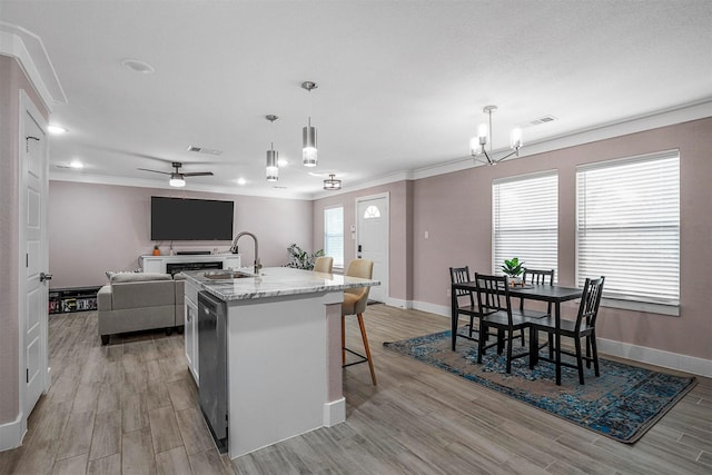 kitchen with a sink, visible vents, ornamental molding, an island with sink, and pendant lighting