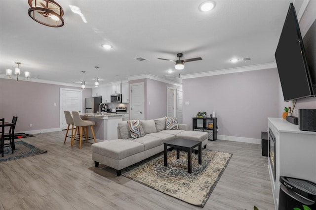 living area featuring baseboards, ornamental molding, and ceiling fan with notable chandelier