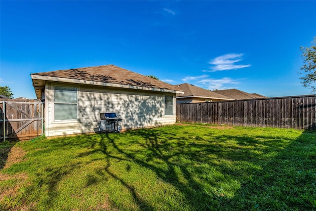 rear view of house with a shingled roof, a yard, and fence