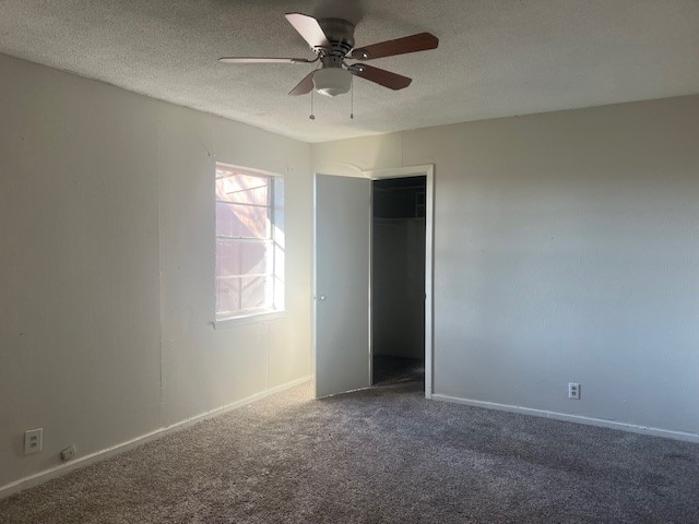 unfurnished bedroom featuring dark carpet, a textured ceiling, a closet, and ceiling fan