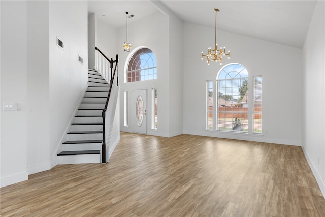 foyer entrance with high vaulted ceiling, an inviting chandelier, and light wood-type flooring