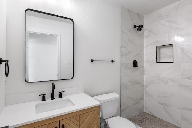 bathroom featuring toilet, a tile shower, and vanity