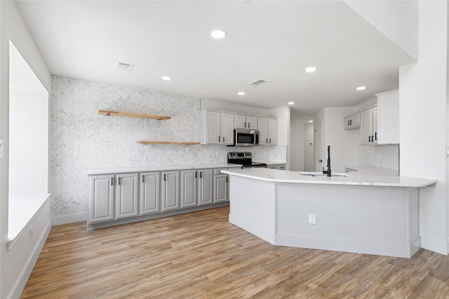 kitchen with appliances with stainless steel finishes, sink, kitchen peninsula, and light hardwood / wood-style flooring