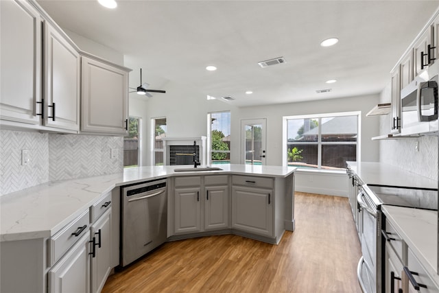 kitchen featuring appliances with stainless steel finishes, tasteful backsplash, light hardwood / wood-style floors, sink, and ceiling fan