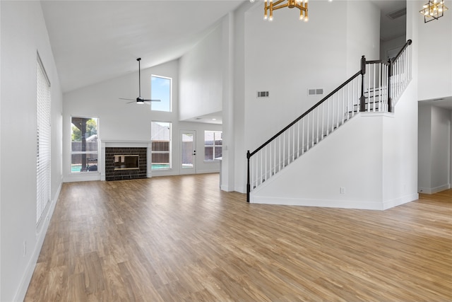 unfurnished living room featuring high vaulted ceiling, wood-type flooring, a wealth of natural light, and a brick fireplace