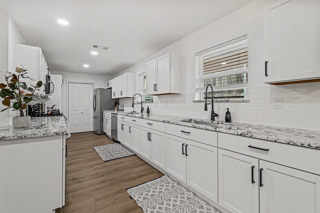 kitchen with white cabinets, hardwood / wood-style floors, appliances with stainless steel finishes, sink, and tasteful backsplash