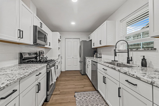 kitchen with backsplash, light hardwood / wood-style flooring, stainless steel appliances, white cabinetry, and sink