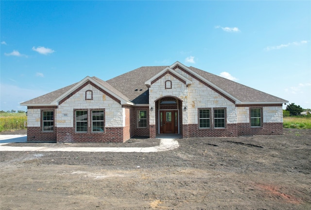 view of front of home with stone siding, brick siding, and roof with shingles