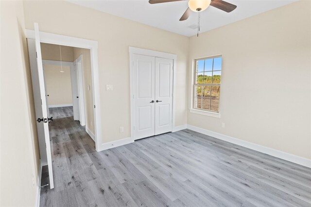 unfurnished bedroom with wood finished floors, a closet, baseboards, attic access, and ceiling fan