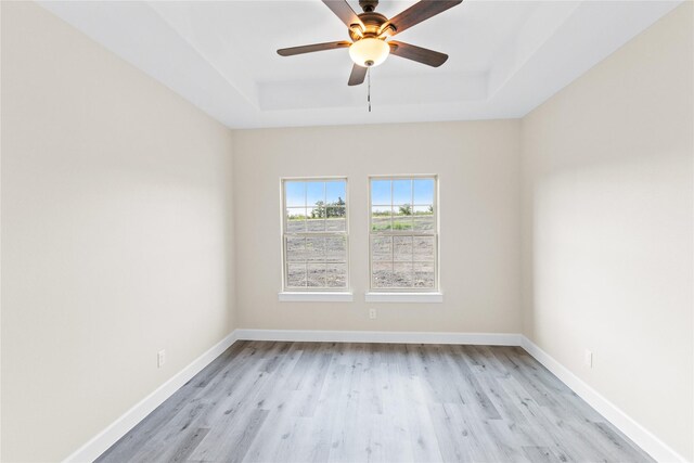 spare room with light wood-style floors, a raised ceiling, and baseboards