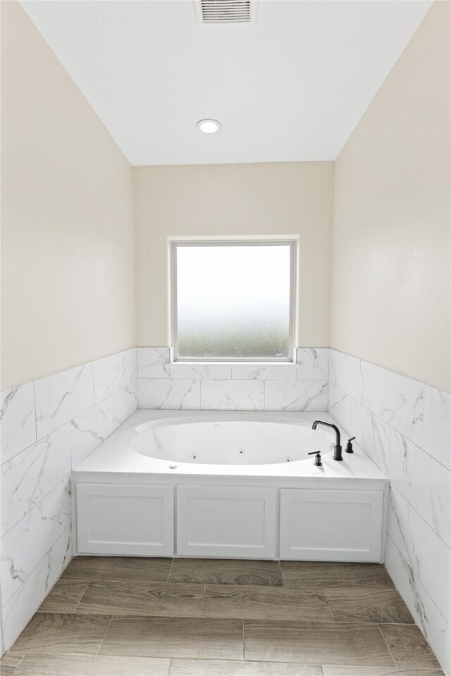 bathroom with visible vents, wood tiled floor, a wainscoted wall, a whirlpool tub, and tile walls