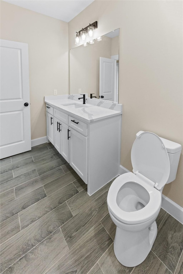 bathroom featuring toilet, vanity, baseboards, and wood tiled floor