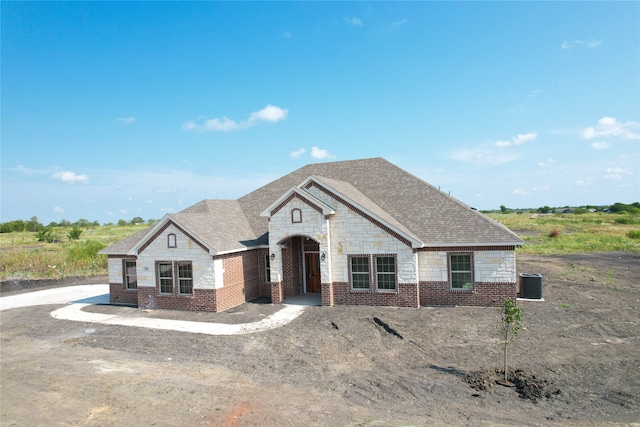 french provincial home with brick siding, stone siding, and a shingled roof