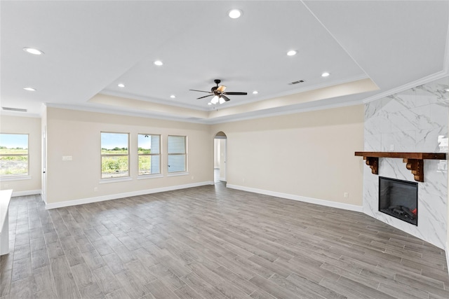 unfurnished living room with a ceiling fan, wood finished floors, arched walkways, a premium fireplace, and a raised ceiling