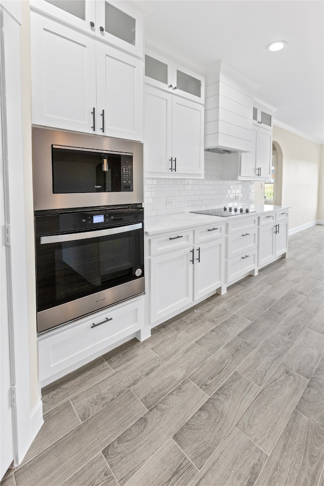 kitchen featuring appliances with stainless steel finishes, decorative backsplash, premium range hood, and white cabinetry