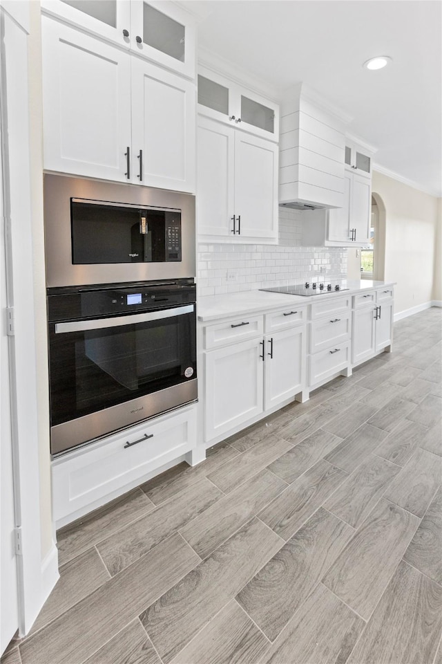 kitchen with backsplash, white cabinetry, light countertops, stainless steel oven, and built in microwave