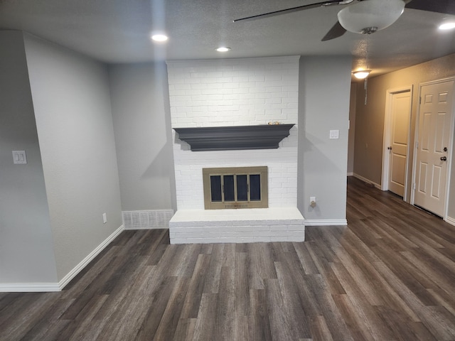 unfurnished living room with a fireplace, dark wood-type flooring, brick wall, and ceiling fan