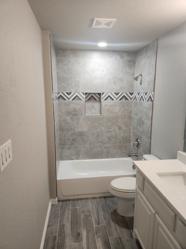 full bathroom with a textured ceiling, vanity, toilet, and tiled shower / bath