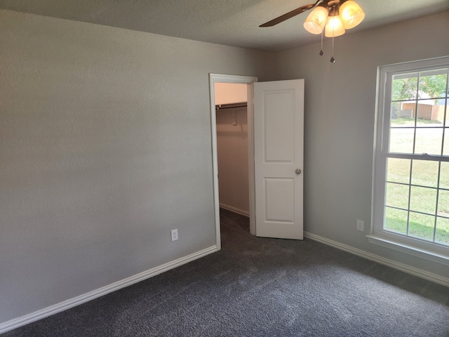 unfurnished room with a textured ceiling, dark colored carpet, and ceiling fan