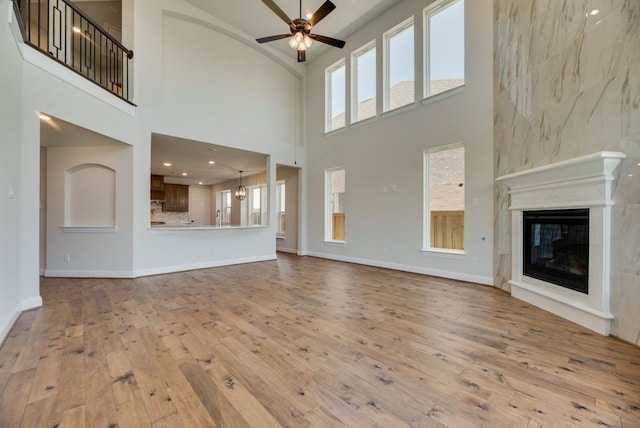 unfurnished living room featuring ceiling fan, a large fireplace, a towering ceiling, and light hardwood / wood-style flooring