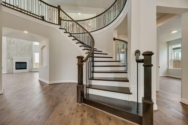 staircase with hardwood / wood-style floors, a high end fireplace, a high ceiling, and baseboards