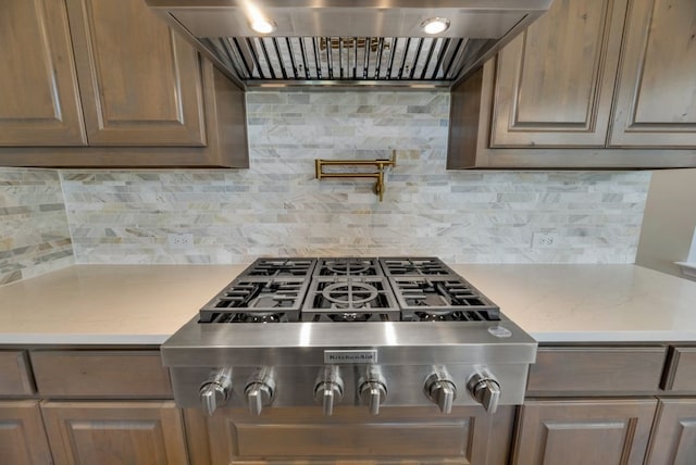 kitchen with light stone countertops, custom range hood, decorative backsplash, and stainless steel gas stovetop