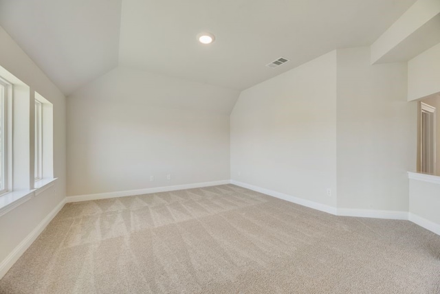 spare room featuring light colored carpet, vaulted ceiling, visible vents, and baseboards