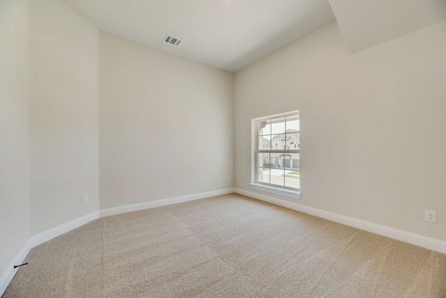 spare room featuring visible vents, vaulted ceiling, light carpet, and baseboards