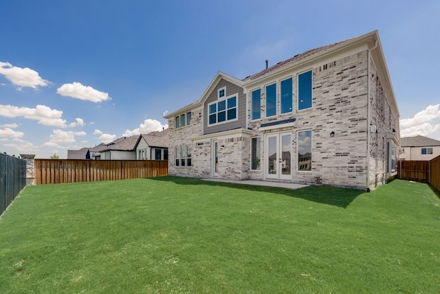 rear view of house with french doors, a fenced backyard, and a lawn