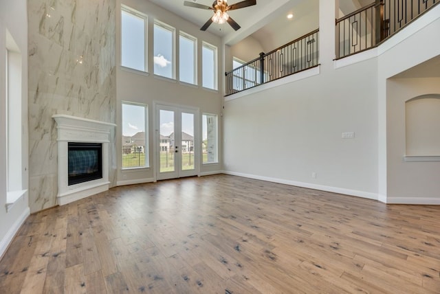 unfurnished living room featuring baseboards, a glass covered fireplace, wood-type flooring, ceiling fan, and french doors